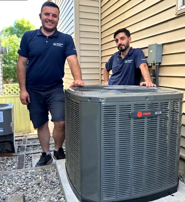 Two Pro West technicians in uniform beside a freshly installed Trane outdoor unit